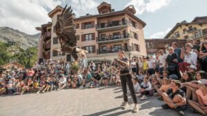 A summer crowd watches a live bird of prey demonstration in Arc 1950, with a large eagle flying close to the camera and traditional Alpine buildings in the background.