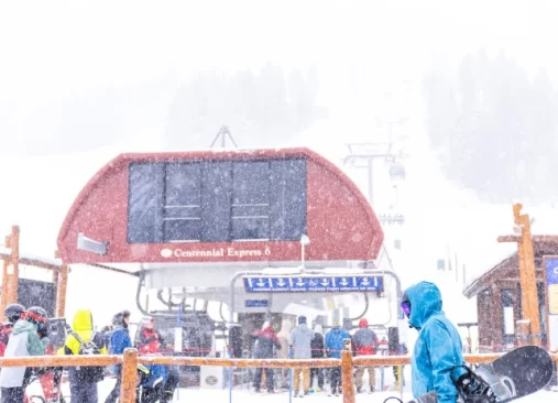 a red chair lift base station is pictured through thick snow falling and a dozen people loading