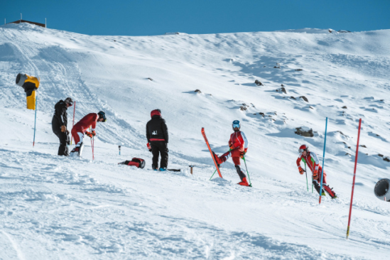 ski racers chilling out, one with ski on tail end, others leaning on poles 