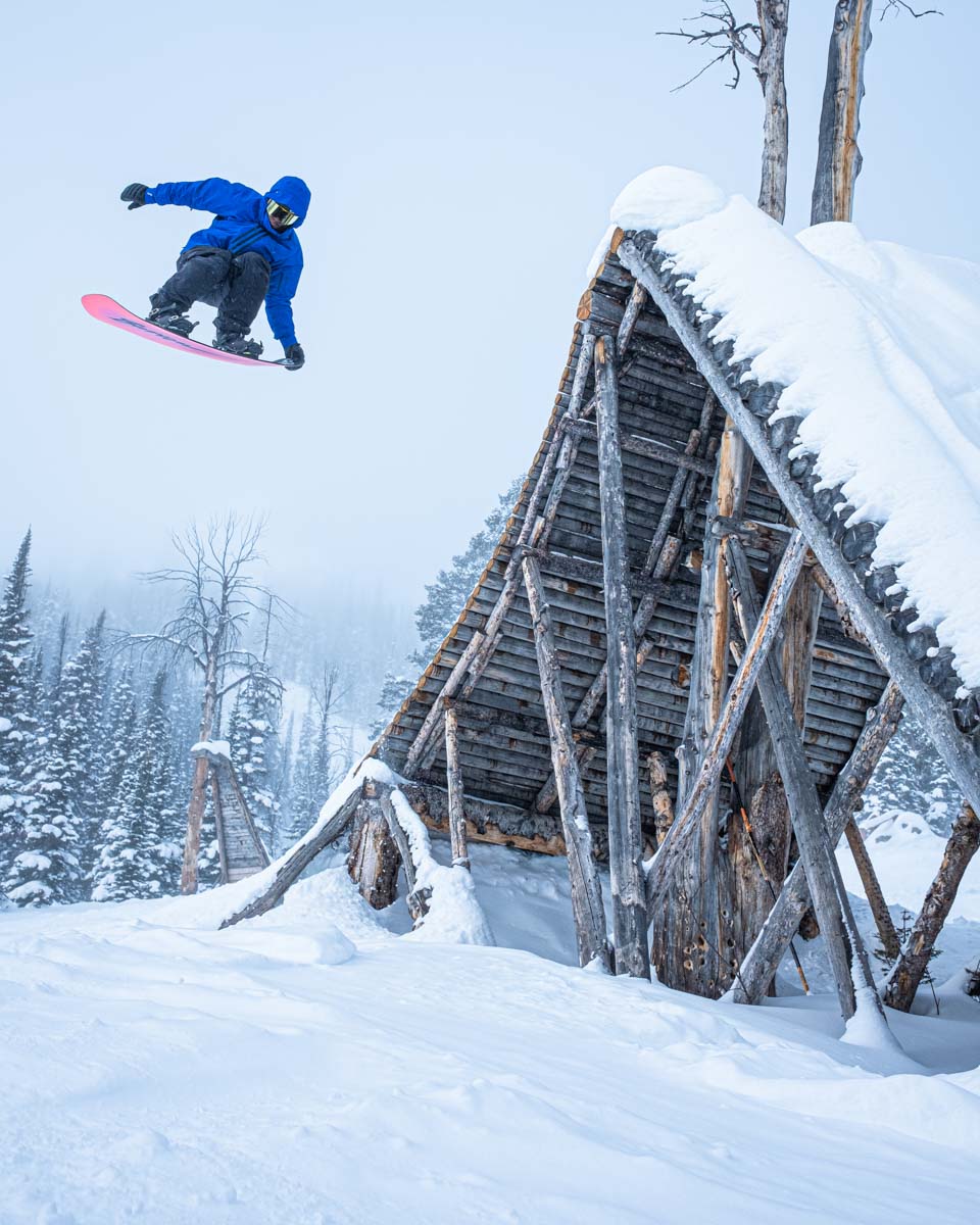 a snowboarder taking big air off a snow-covered wood feature on a snowy day 
