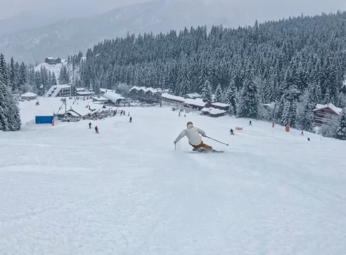 a skier carves on a slope leading to a lift base station and village, covered in snow