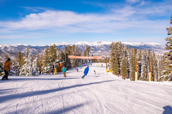a gentle green or blue slope is skied and snowboarded on by a handful of people in a resort's opening day picture in the USA