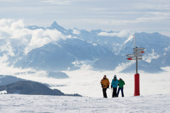 three skiers stand by a sign post on the mountain, with an epic mountain view