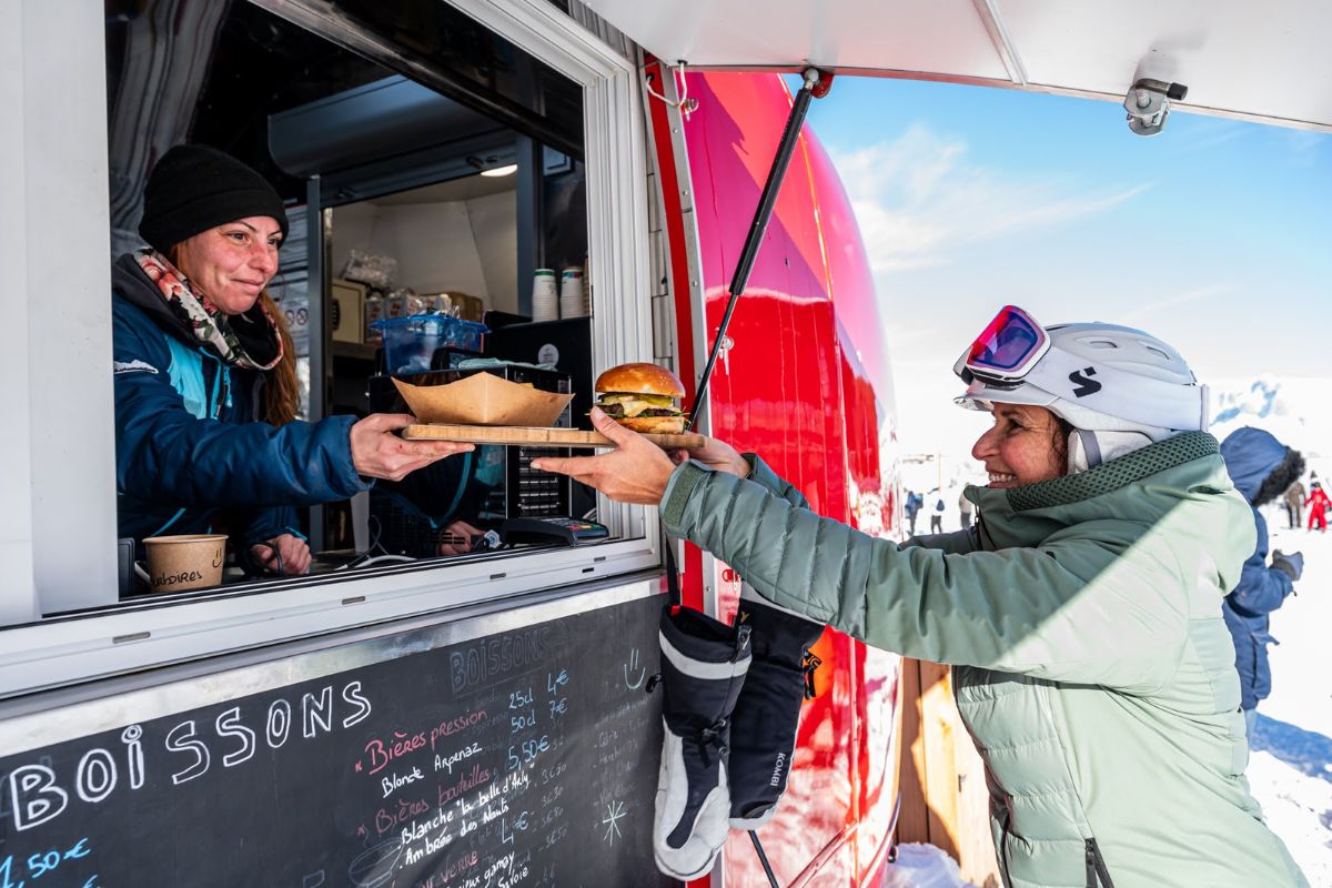 Skier receiving a gourmet burger from a mountain food truck in Les Portes du Mont Blanc