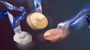 A dynamic image of the Olympic medals in motion, their textures catching the light. The iconic Milano Cortina 2026 ribbon swirls through the air, adding a sense of celebration and movement to the medal design.