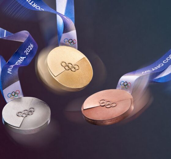 A dynamic image of the Olympic medals in motion, their textures catching the light. The iconic Milano Cortina 2026 ribbon swirls through the air, adding a sense of celebration and movement to the medal design.