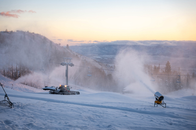 snow making in action at dusk on the mountain with snow cannon and c-groomer
