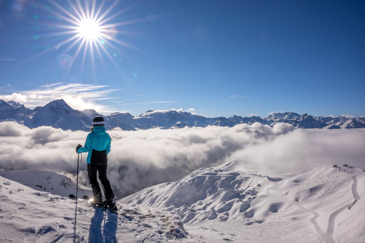 Skier overlooking the terrain served by the Roche de Mio Gondola in La Plagne with clouds and alpine peaks in view.