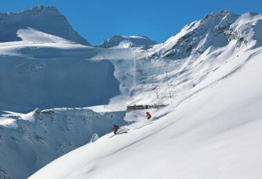 Skiers descending near Rettenbach glacier with lift infrastructure in background