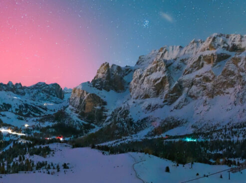 a (possibly AI modified) image of snowy mountains at night, with sars visible and a pink sky