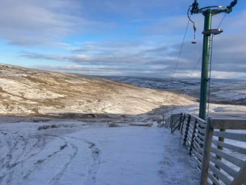A snow fence is pictured, above it a stationary button lift, with a thin cover of snow on the ground - the picture is of a Scotland ski hill