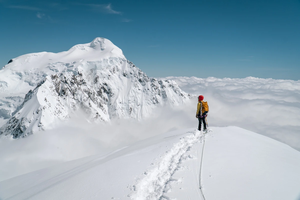 a solo skier standing at the top of the world, or on Mt Cook, under a blue sky surrounded by white peaks