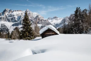 a metre of snow sits on the roof of a tiny wood hut, the mountain across the valley looking huge and beautiful beyond the hut