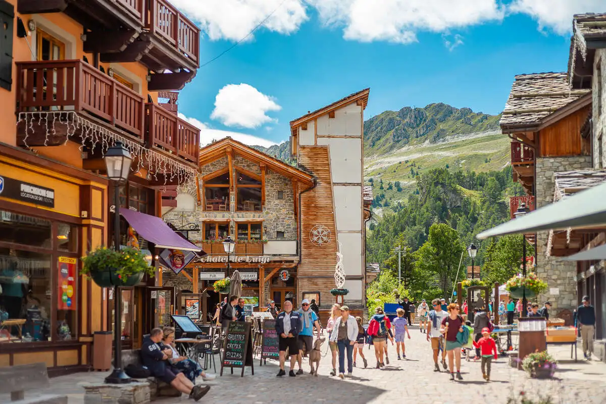 an alpine village centre photographed in summer with rocky, grassy steep slopes of mountain tops beyond buildings