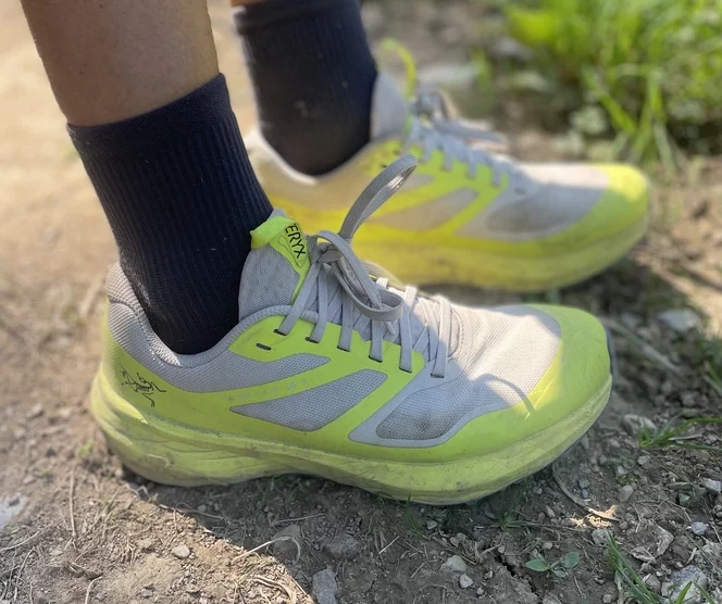 yellow and grey trail shoes, photographed from the wearer, down to the dry earthy ground