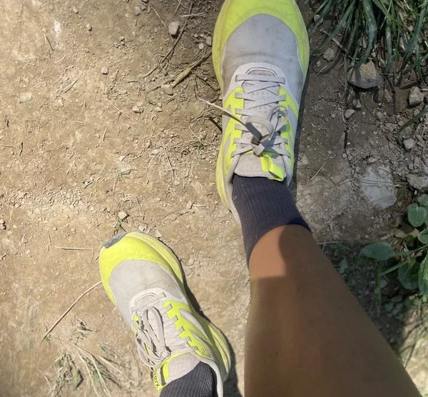 yellow and grey trail shoes, photographed from the wearer, down to the dry earthy ground