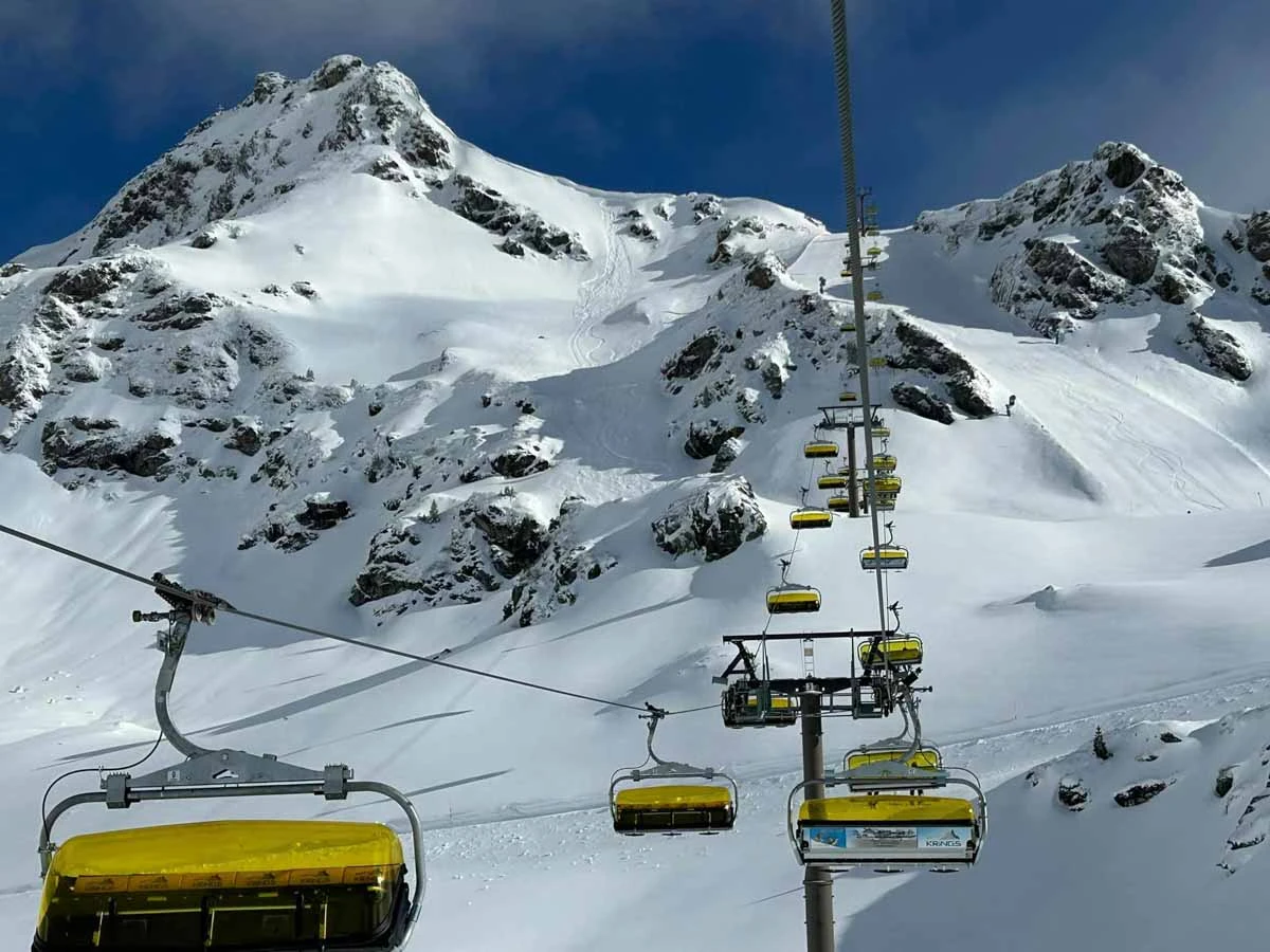 a yellow-bubbled chair lift if pictured over fresh snow and a piste with just two fresh tracks, high in the mountains
