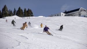 a group of young-looking skiers make fresh tracks down a mellow piste, skiing close together