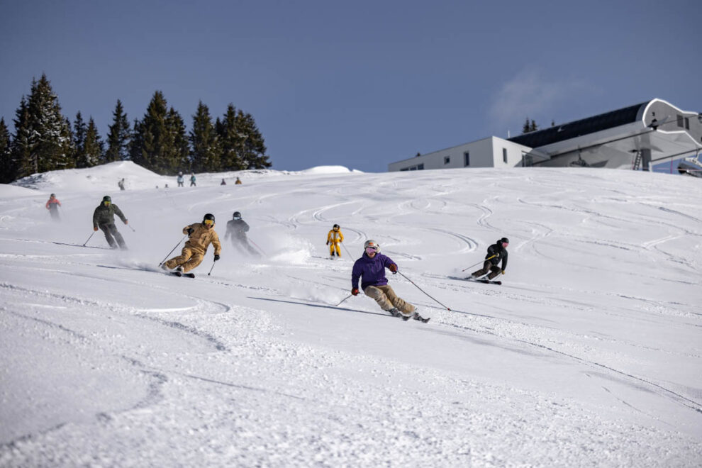 a group of young-looking skiers make fresh tracks down a mellow piste, skiing close together