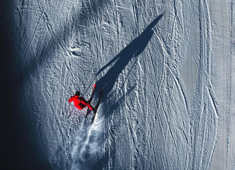 a drone shot of a skier in red carving, their shadow huge