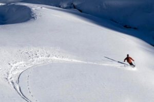 a lone skier makes fresh tracks on untouched, heavy sun-affected snow