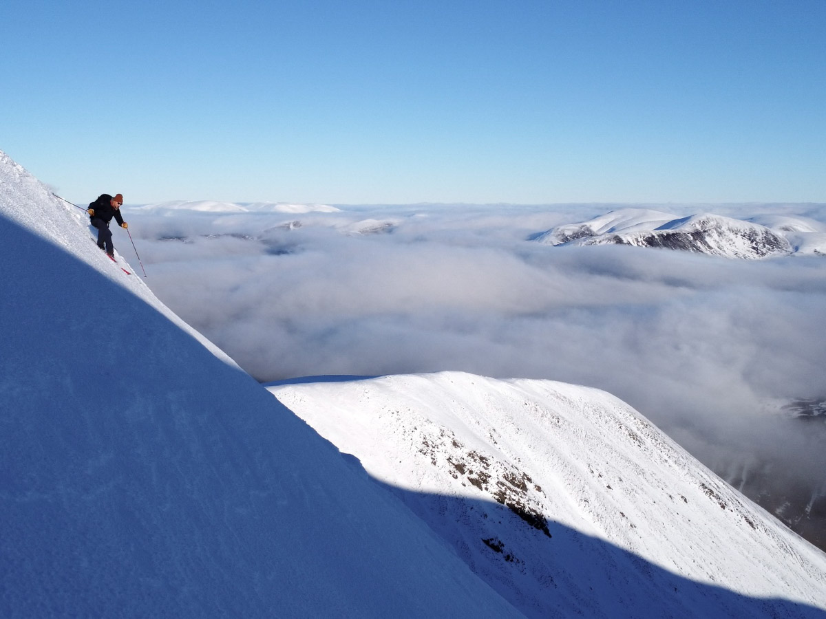 the shadow line running along a high Scottish mountain, a skier silhouetted stands over the sunny side, about to ski a steep