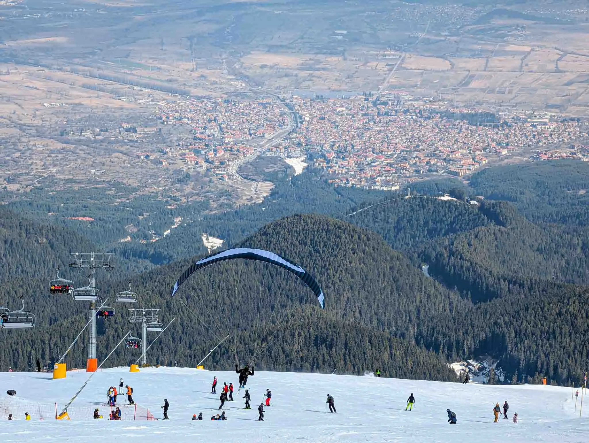 a paraglider takes off from a busy piste, the snowless valley the picture focus far below