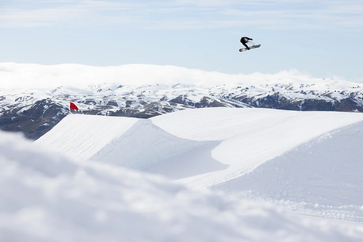 a snowboarder high in the air, having taken off an enormous kicker
