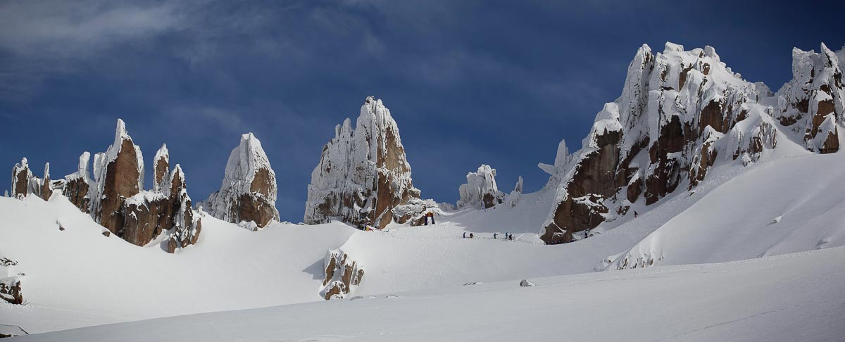 spire-like mountain peaks, covred in rime ice, with ant-sized skiers hiking to the snowy feet of the jagged rocks