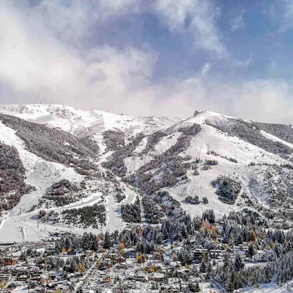 a dusting of snow covers a ski village and its ski runs cut into the alpine