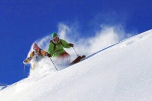 two skiers off-piste, against a bright blue sky