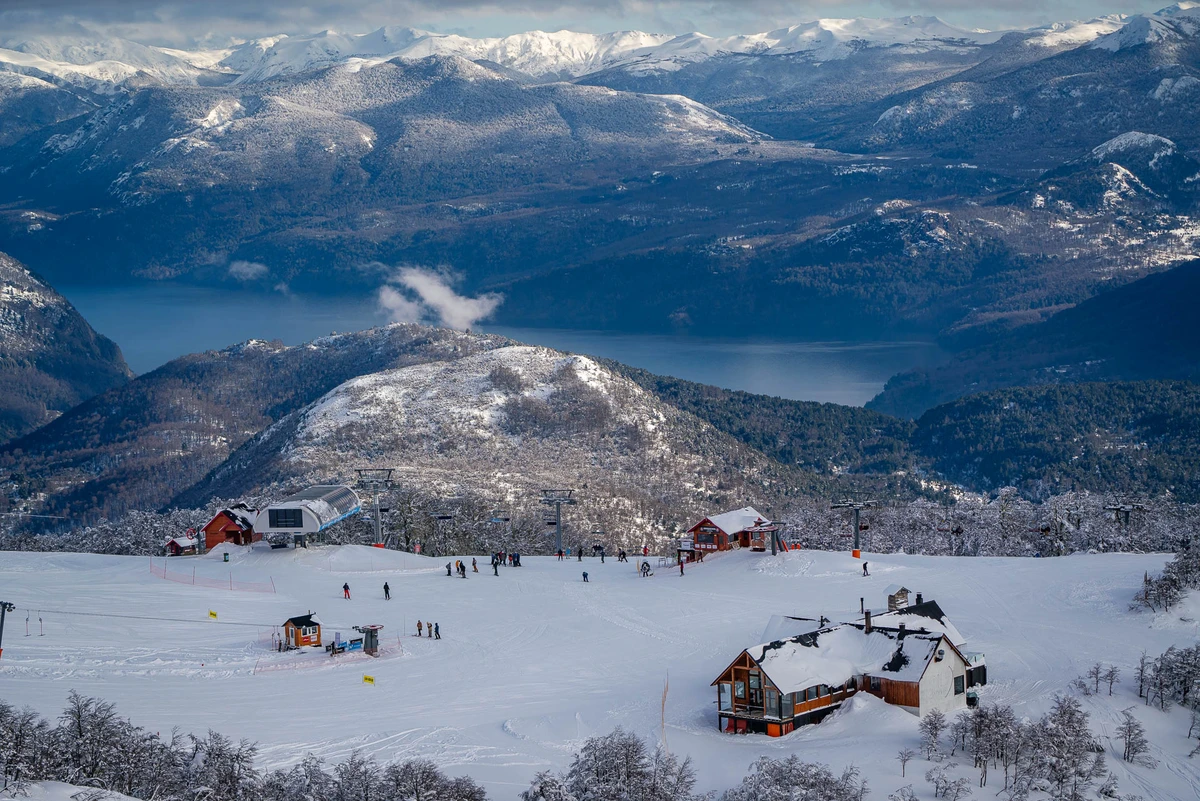 a mid-mountain ski area with several building and a lift station overlooking a lake in the valley below