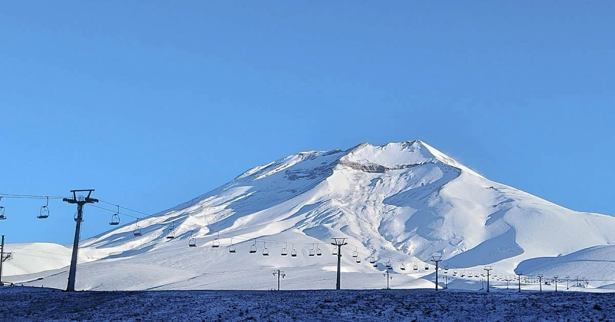 a flat plain and single mountain covered in snow, with a single chairlift travelling the flat ground