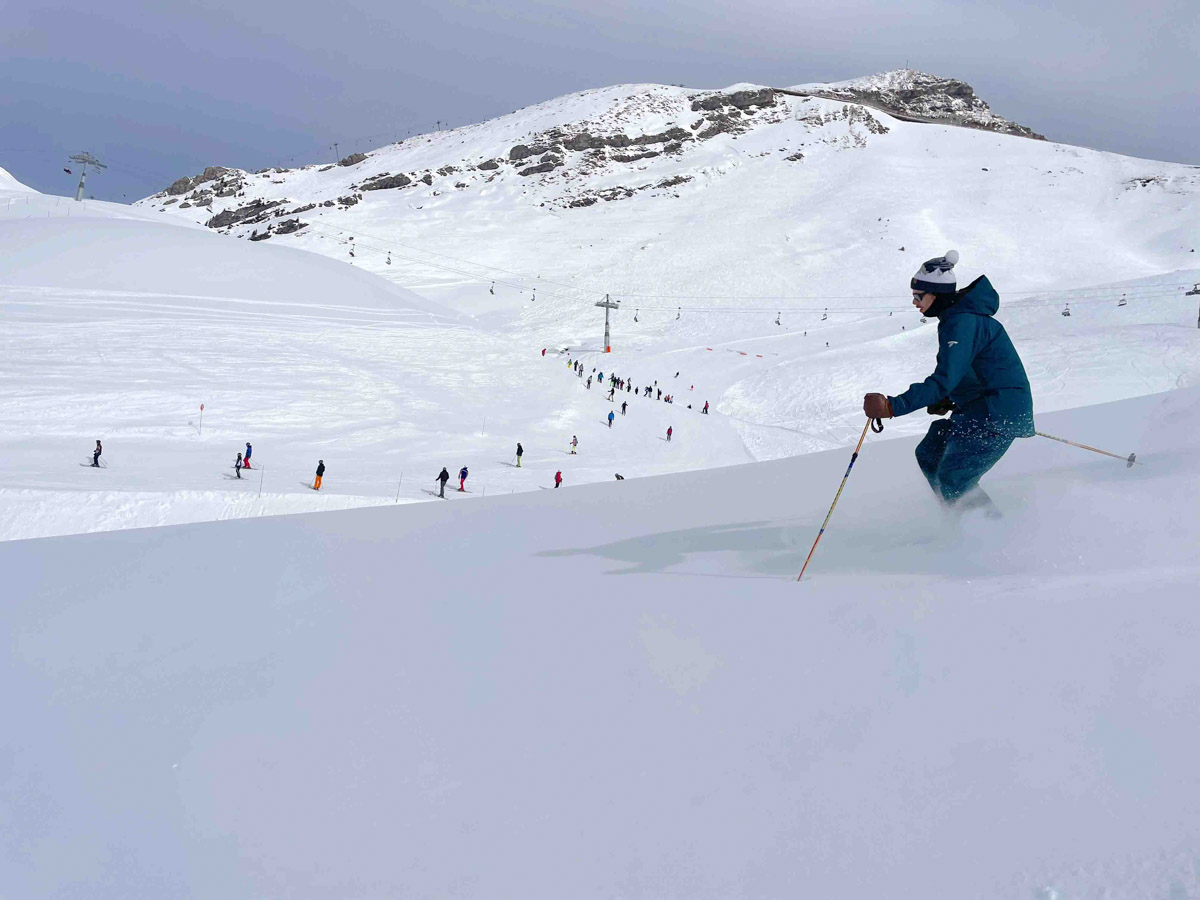 skier skis in mellow off piste, with the ski resort piste and skiers visible just beyond