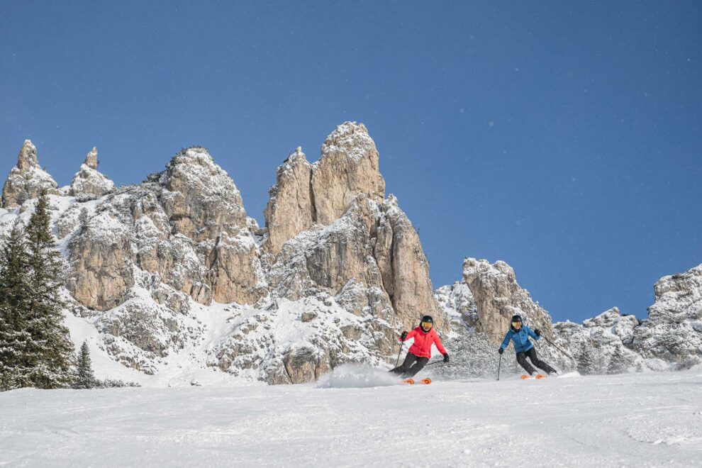 two skiers carving under Dolomite mountain peaks