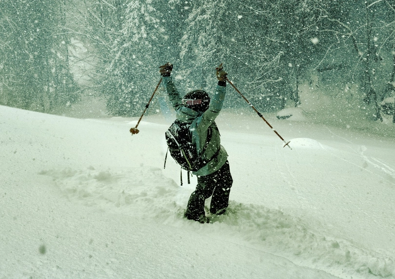 a skier celebrates, arms up, standing in deep pow, perhaps at night with a green glow to the scene