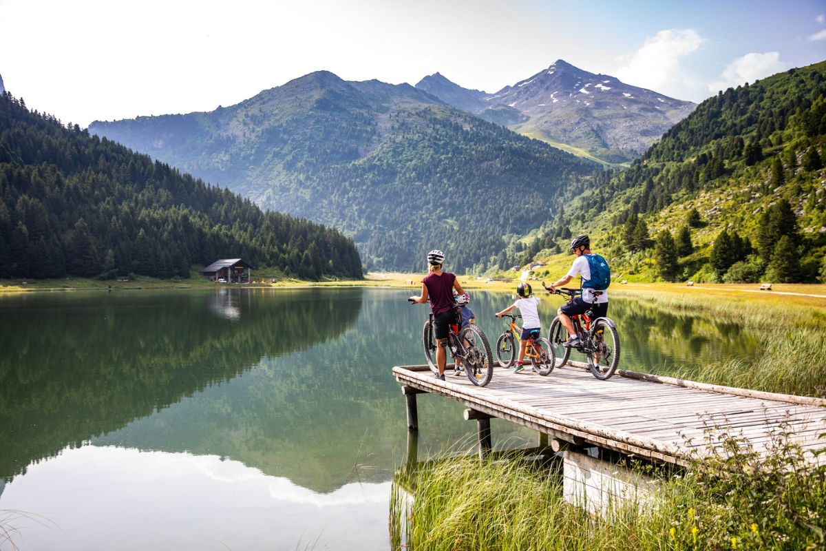Family cycling near a lake in Méribel with forest and alpine peaks in the background