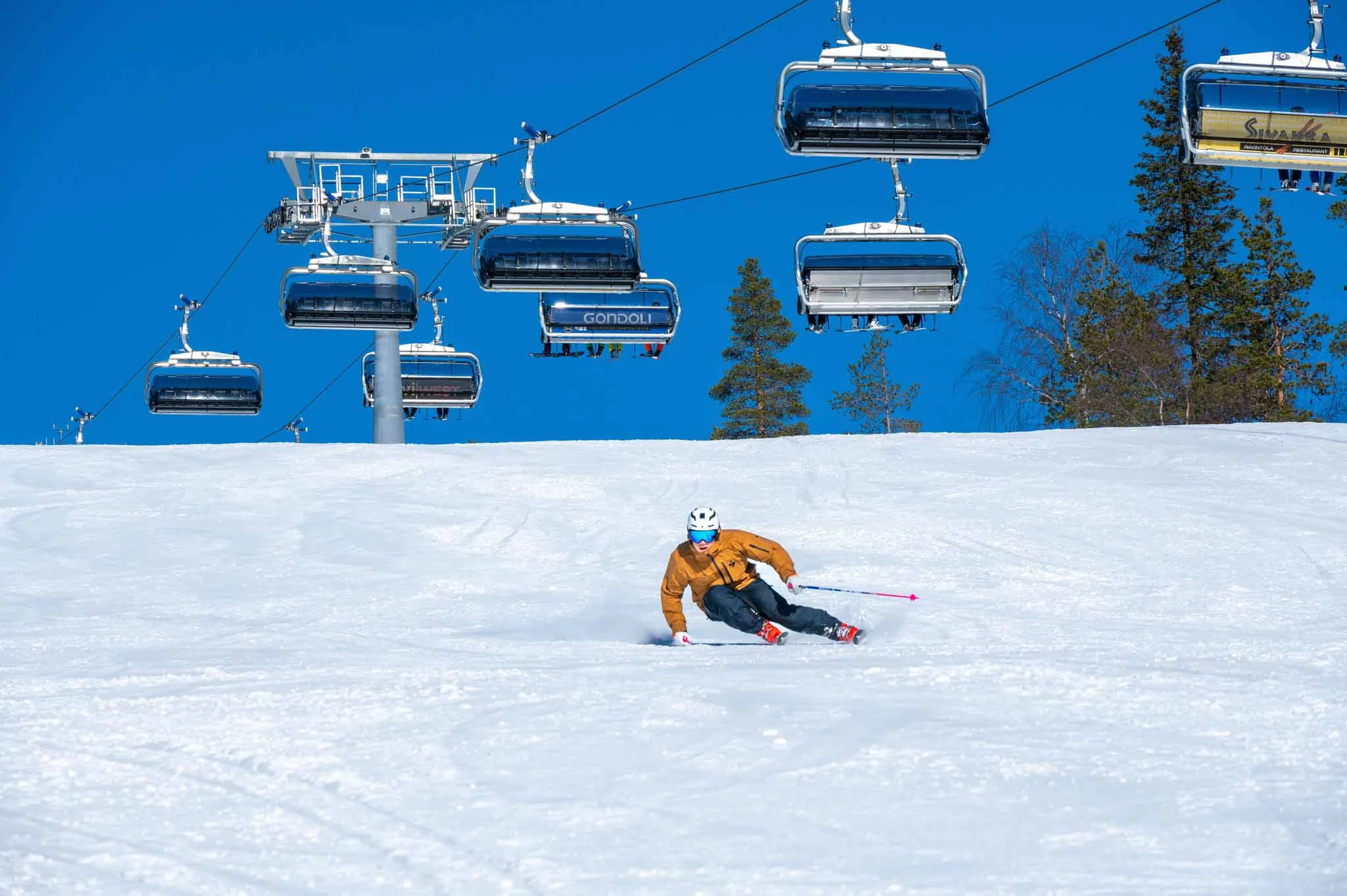 blue sky, empty chairlift with bubble overhead, empty piste, with one skier in orange carving deeply