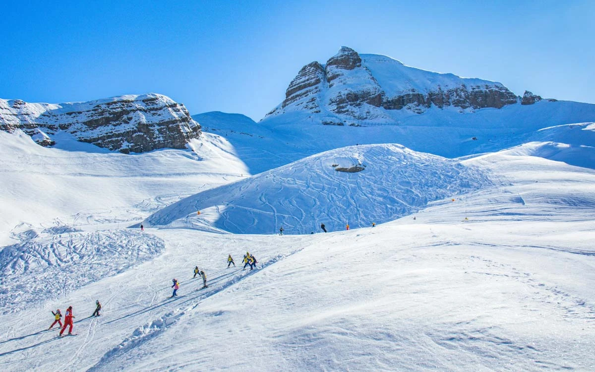 ski school follows instructor down an empty piste in a sunny ski area