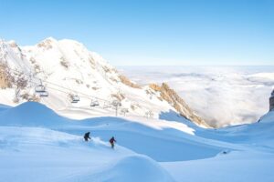 blue sky, fresh snow, two skiers enjoying a 10/10 ski scenario, the valley below a sea of cloud