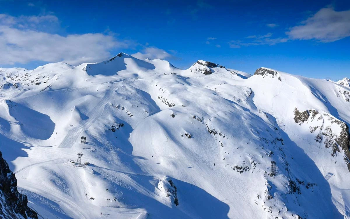 a mountain side is pictured under a blue sky - including all its lifts and pistes looking in great condition