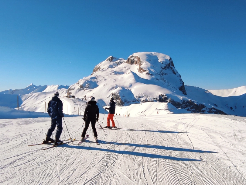three skiers at the top of a mountain on a flat piste, look where to go