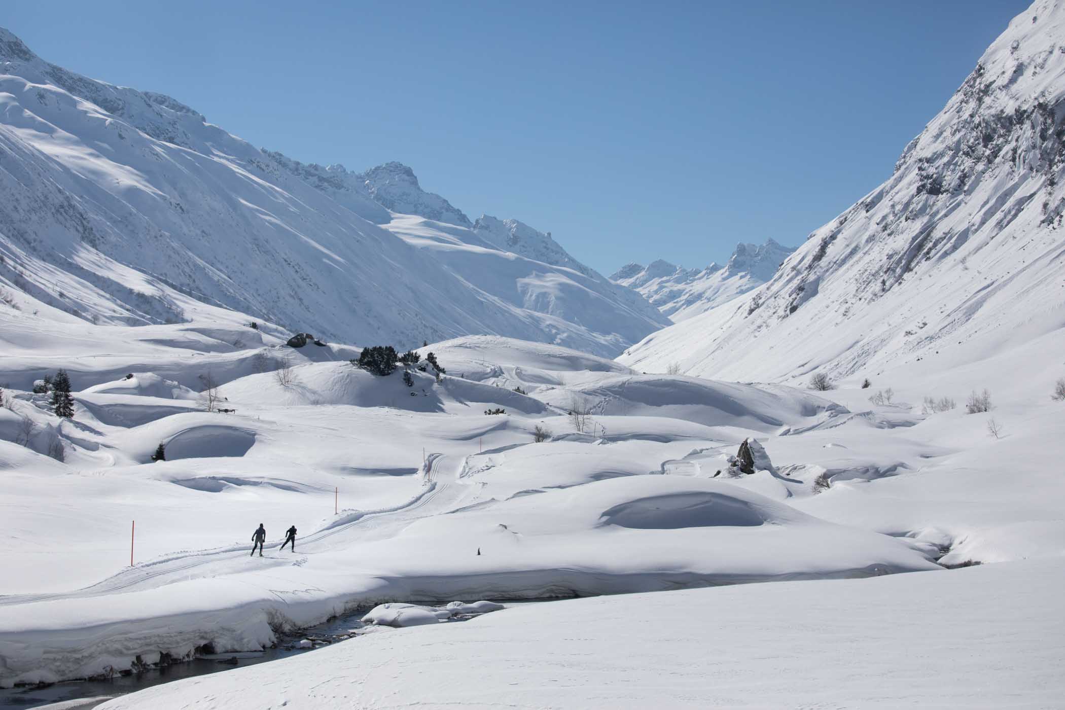 a snowy valley with a cross-country track running through, two skiers on the move