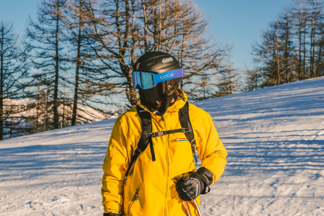 a skier in a yellow jacket and helmet and goggles, looks away from the camera cooly, located on the piste