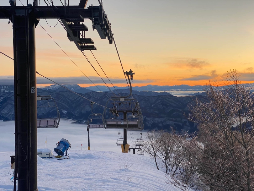 a sunset, with a sleeping ski lift pictured from the top of the mountain, with clouds inverted, filling the valley below