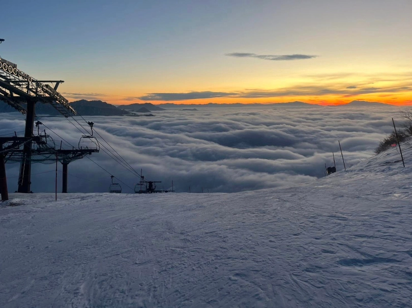 a mountain sunset in the distance over far, high mountains, the picture taken from the top of a piste next to a stand-still chairlift line