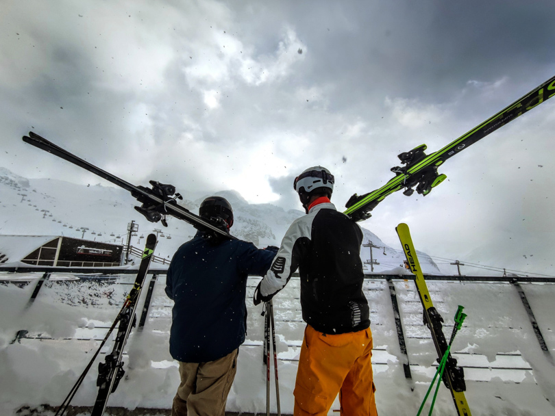 two skiers look out over ski area, skis on shoulders