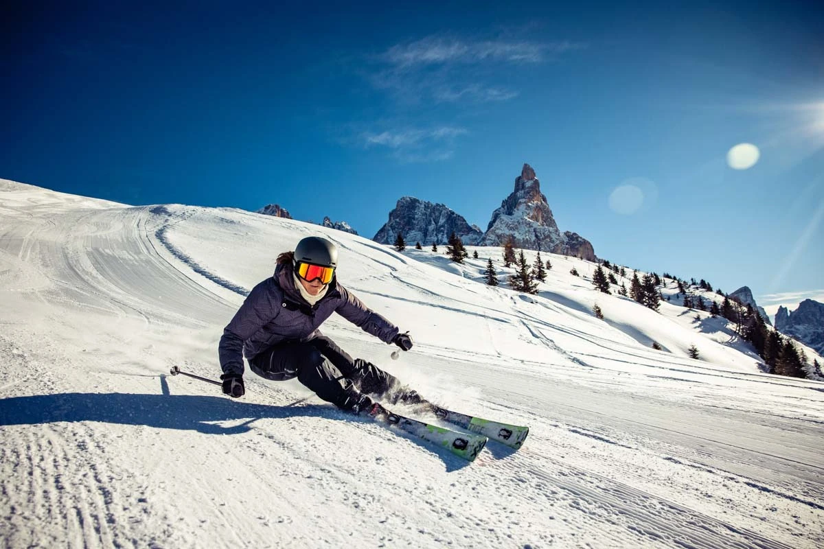 a skier carves deep on a mellow slope, a Dolomites-looking rock rising up sharp in the background