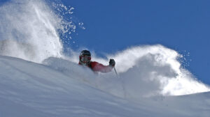 a skier makes a turn in deep pow, sky very blue above