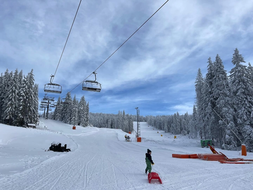 A child dragging a sled on an empty ski piste under a chairlift